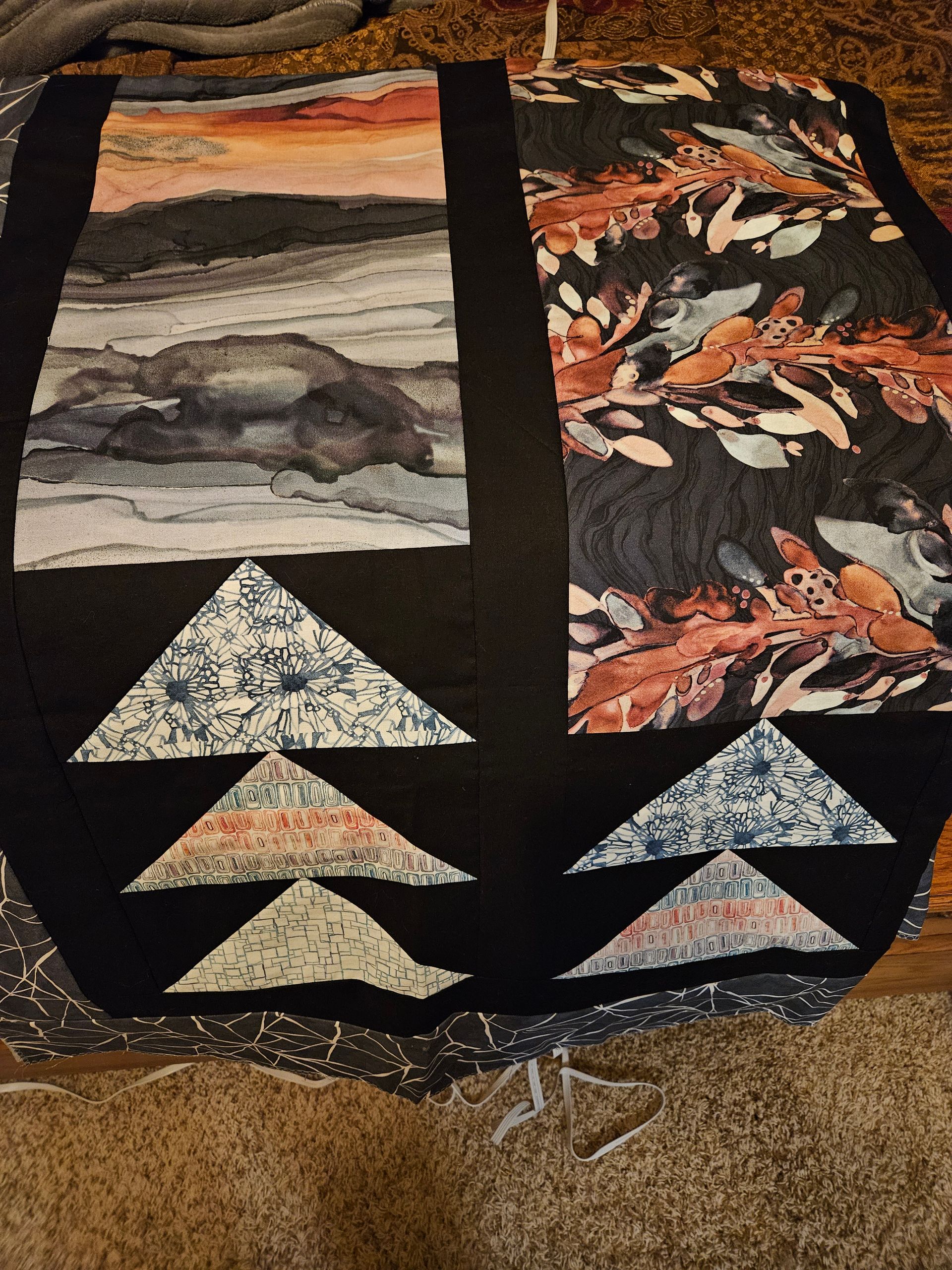 Quilt with autumn trees, sunset landscape, and stacked triangular patchwork on black fabric