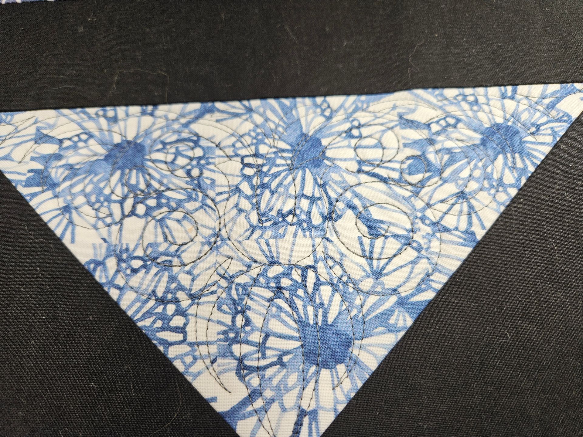 Blue-and-white patterned triangular fabric or paper piece on a dark textured background