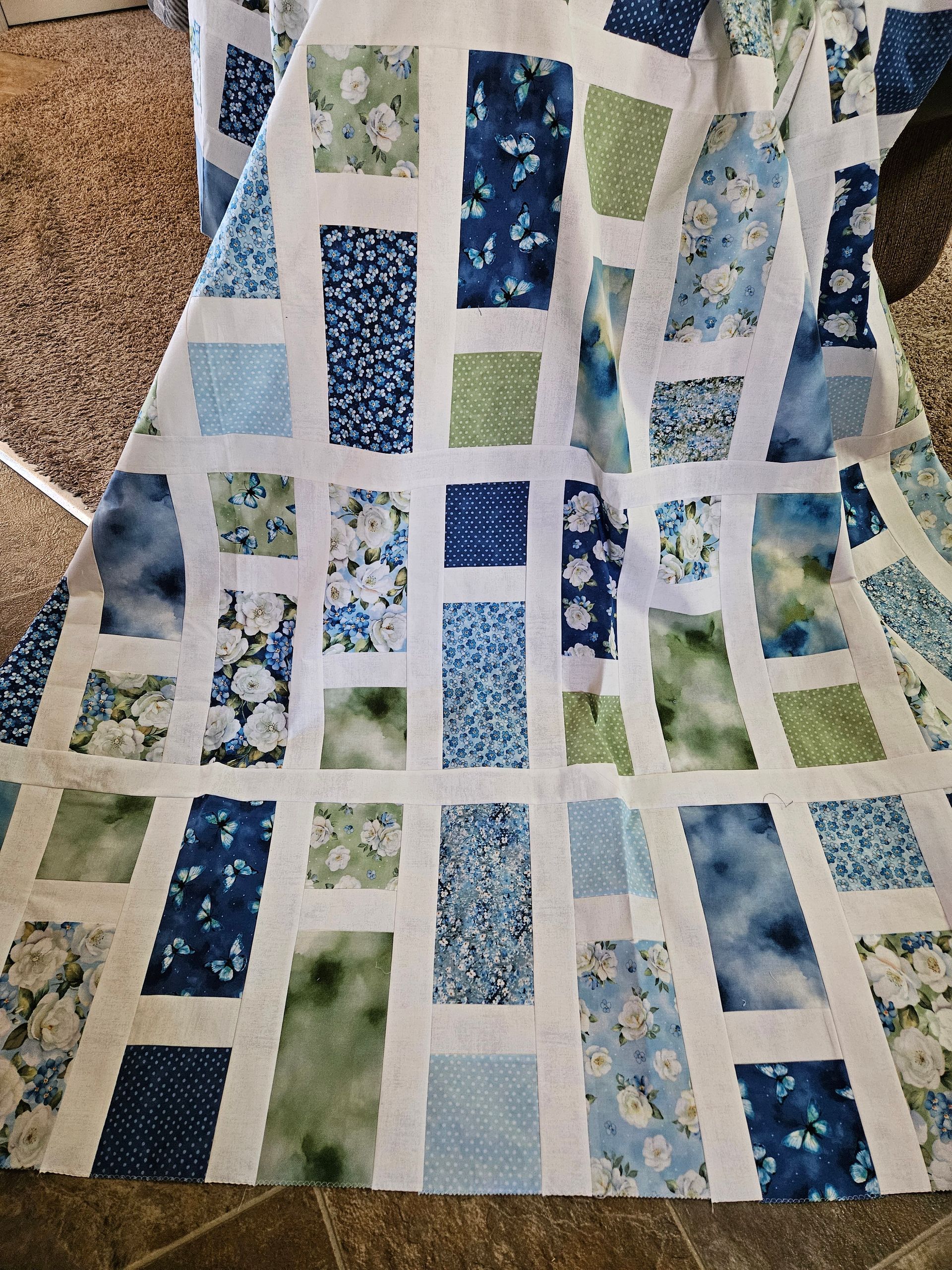 Blue, green, and white patchwork quilt with floral and geometric squares draped over a chair.