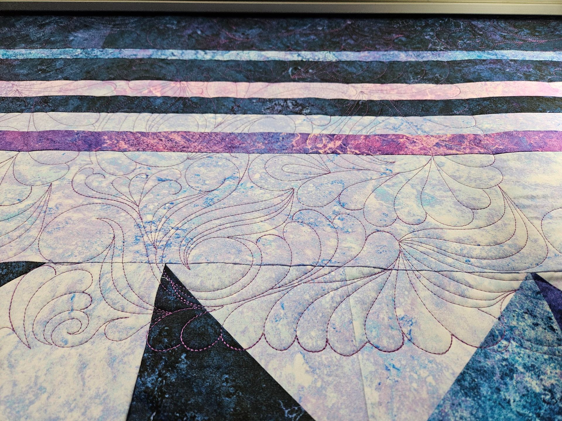 Quilt with swirling floral embroidery in pale blue and purple, bordered by dark and pink horizontal stripes