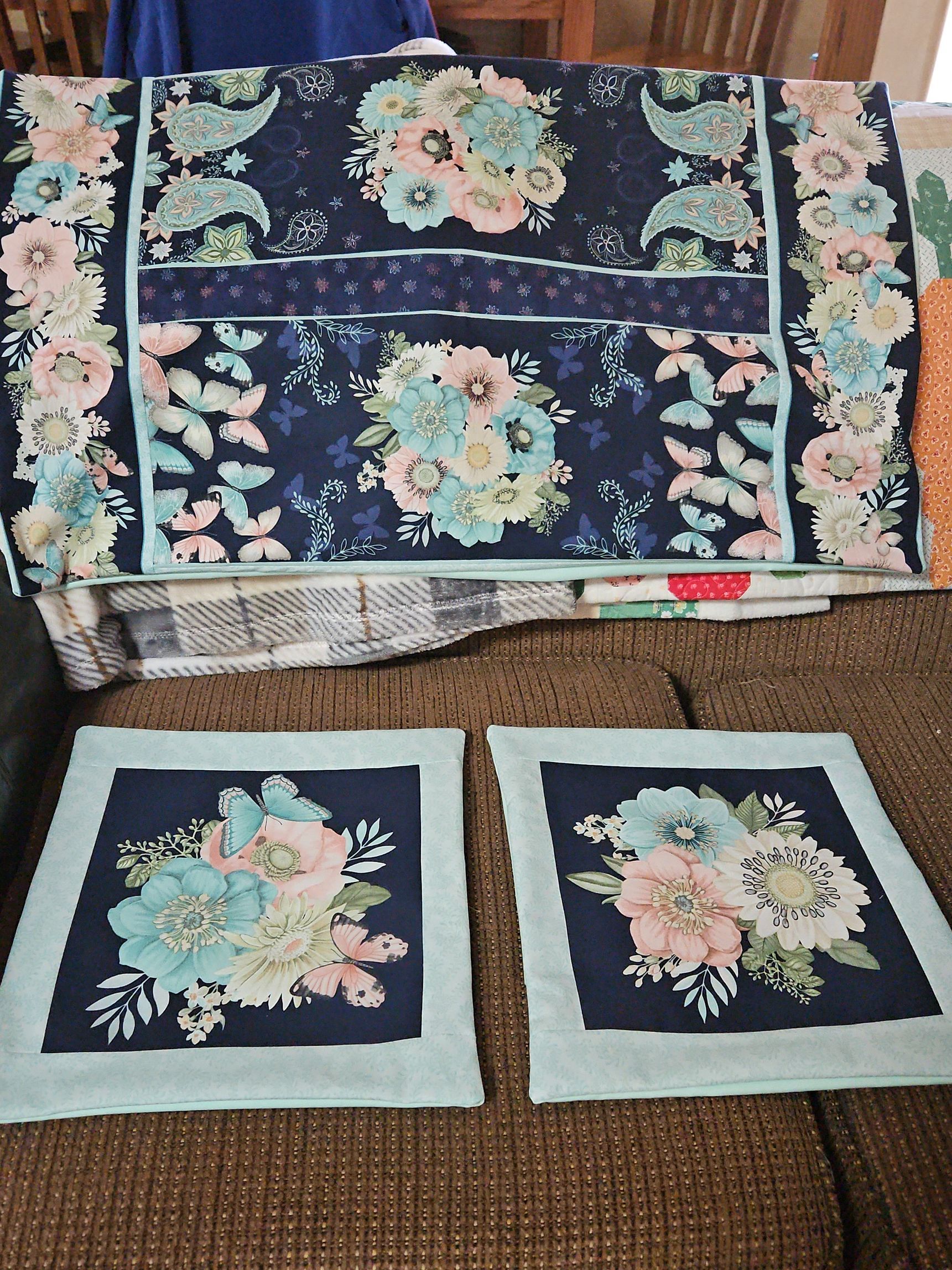 Floral quilted fabric set in navy, teal, and pink, with a matching large piece and two square patches on a brown surface