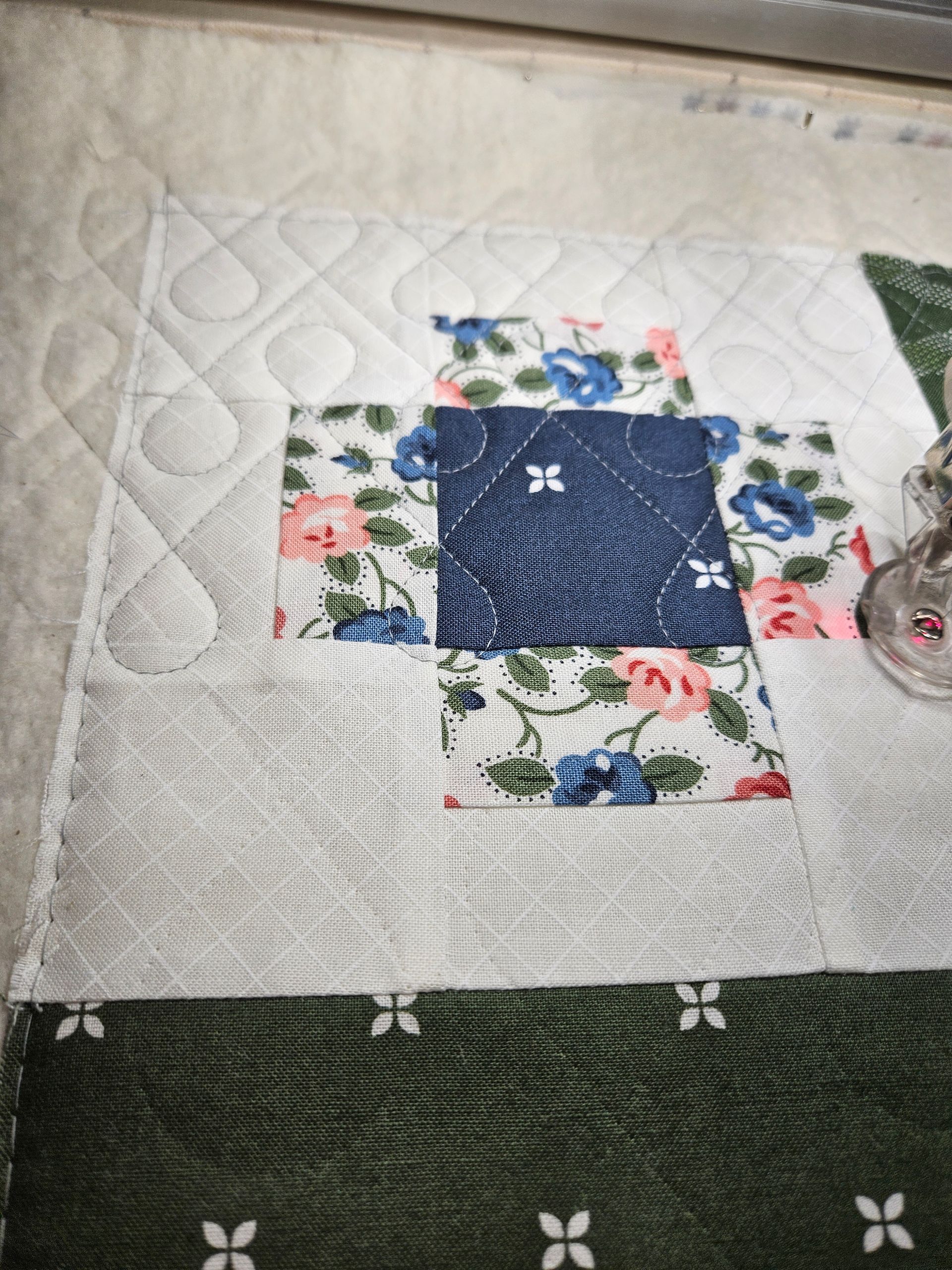 White quilt with a navy floral patchwork square and green border on a tabletop