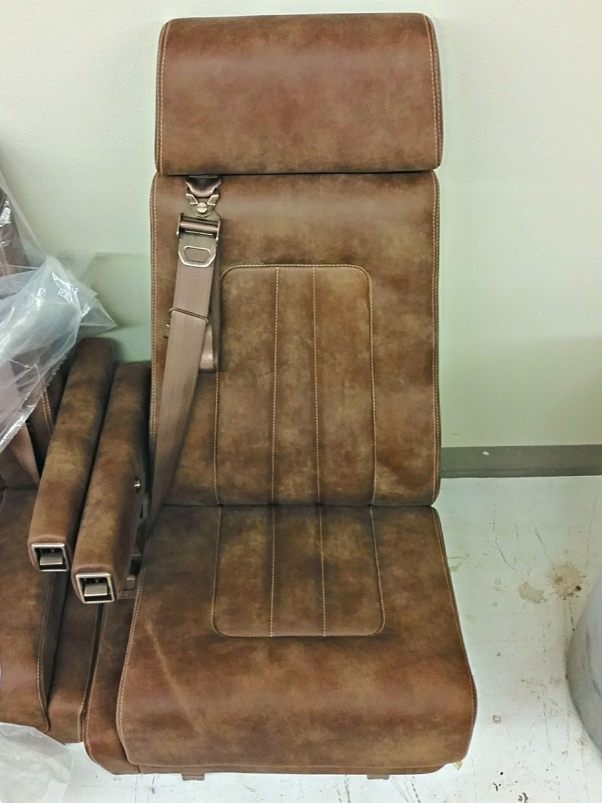 Brown leather car seat upholstery with a shoulder strap visible, shown indoors.