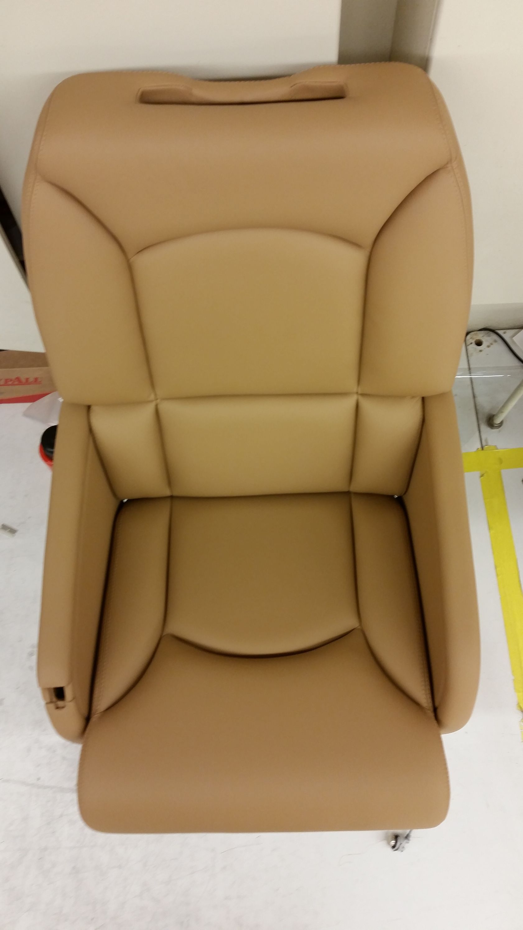 Tan leather car seat on a showroom floor, front view with headrest and armrests