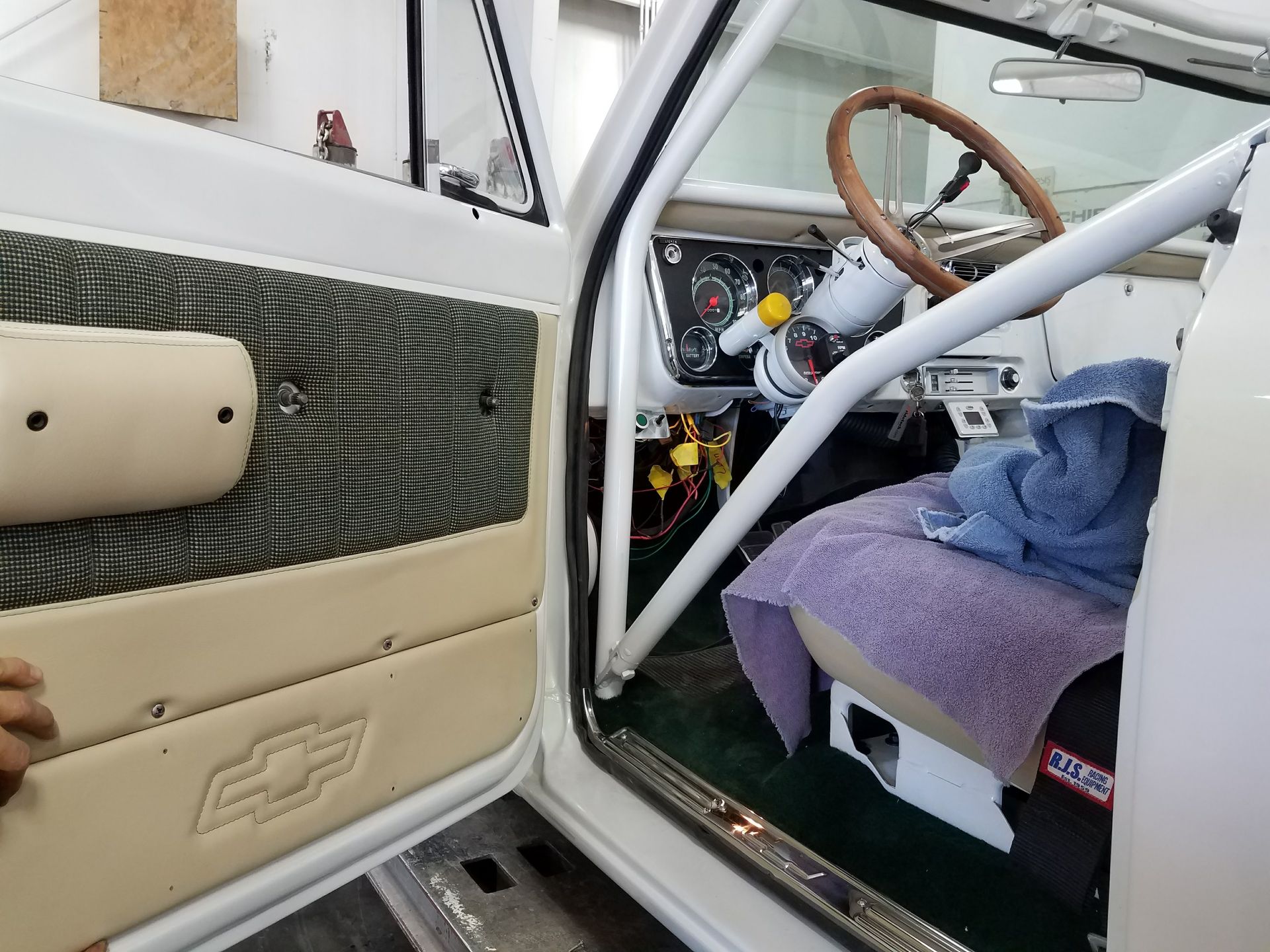 Inside a car, a white roll cage, steering wheel, and beige door panel with a Chevrolet emblem.