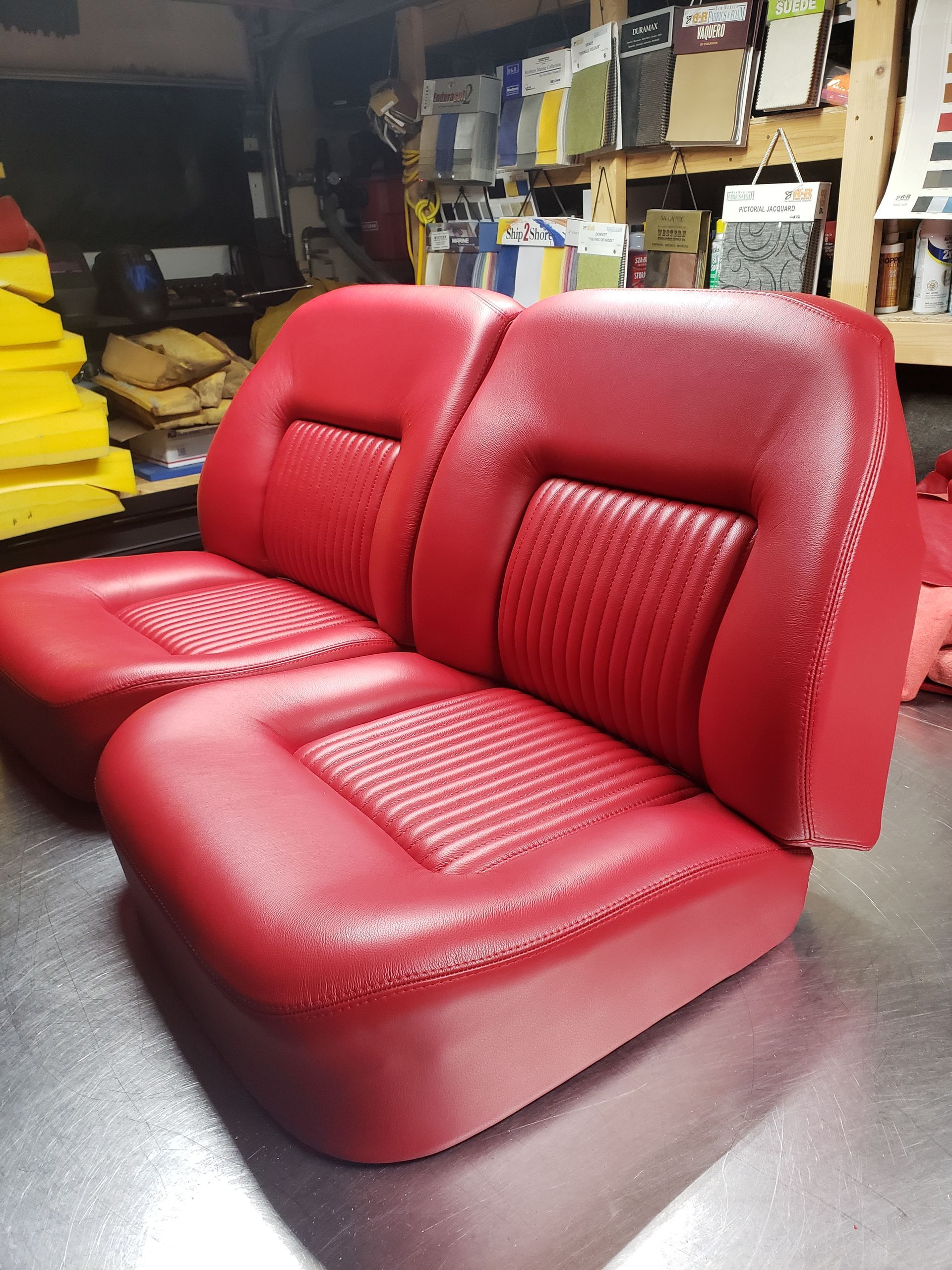 Red leather upholstered car bench seat in a workshop, shown from the front at an angle.