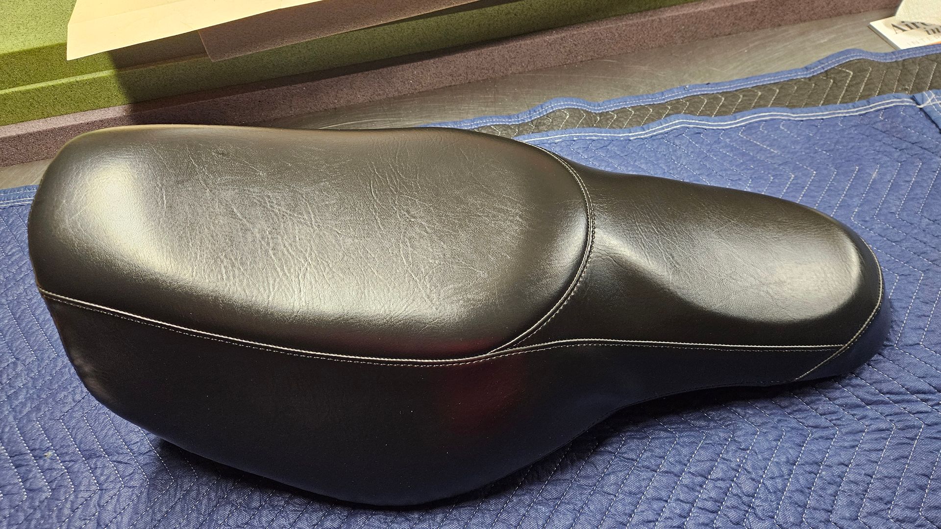Black leather bicycle saddle on a blue textured surface.