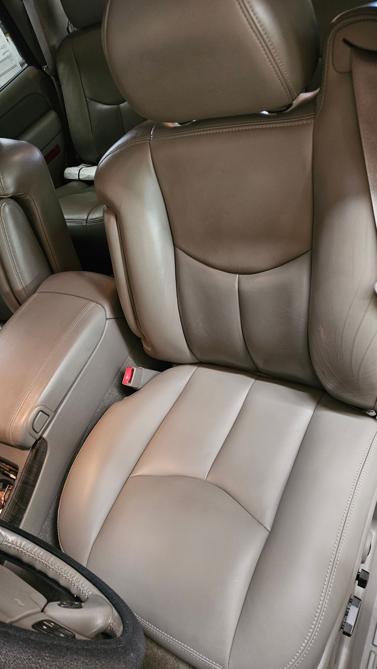 Brown leather car seat with headrest and visible seatbelt buckle in the front interior