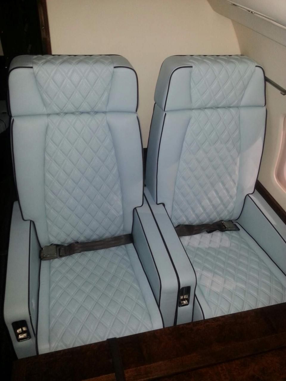 Two light blue quilted airplane seats beside a window, viewed from the aisle.