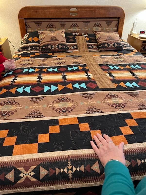 Bed with patterned quilt in earthy tones and turquoise accents; a hand rests on the blanket.