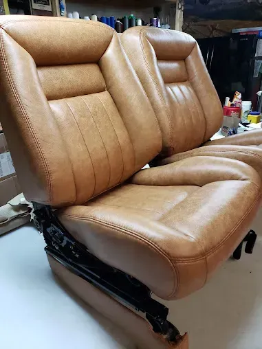Tan leather upholstered car seat on a black metal frame in a workshop