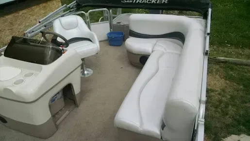 Small pontoon boat interior with cream seating, a steering console, and a blue bucket on the deck.