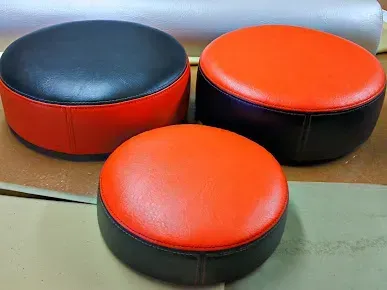 Three round red-and-black cushioned stools on a floor, with a gray bench in the background