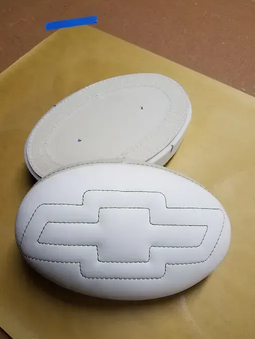 Two white oval foam pads, one with a raised Chevrolet-style cross emblem, on a tan surface.