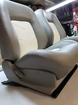 Two beige leather car seats with gray backs, shown in a workshop or garage.