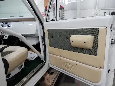 Open car door with beige and gray interior panels and chrome handle