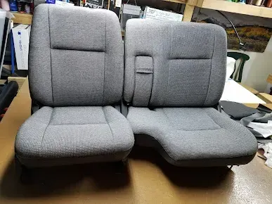 Two gray upholstered car seat cushions with headrests, shown side by side on a workbench.