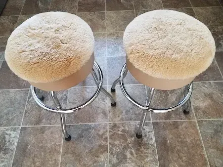 Two round, cream-colored stools with chrome bases on a tiled floor.