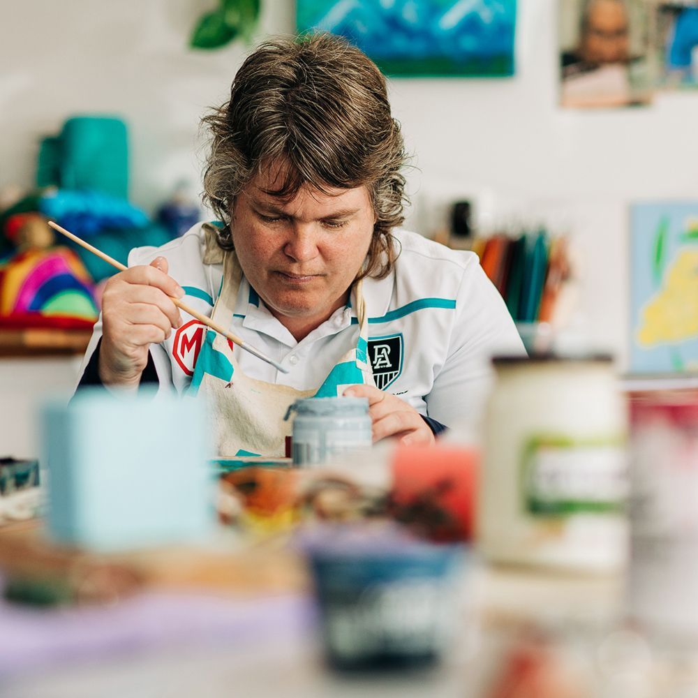 A woman is sitting at a table painting a picture with a brush.