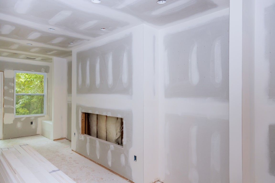 Drywalled room under construction with window light and built-in wall niche above a fireplace opening.