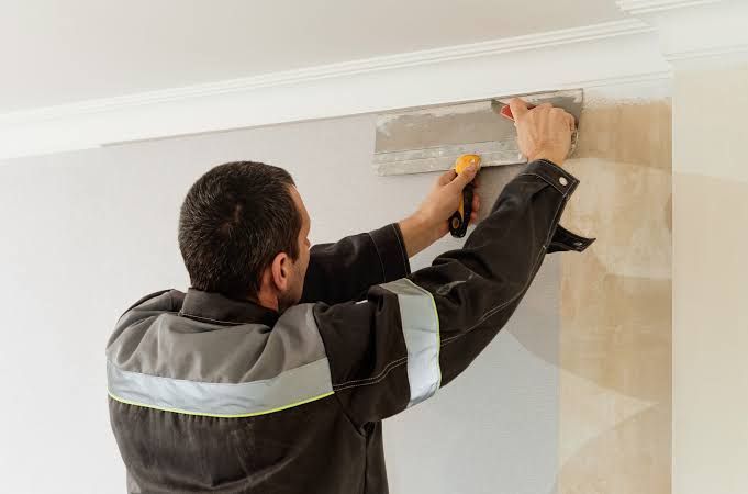 Worker smoothing plaster on a wall with a trowel near the ceiling