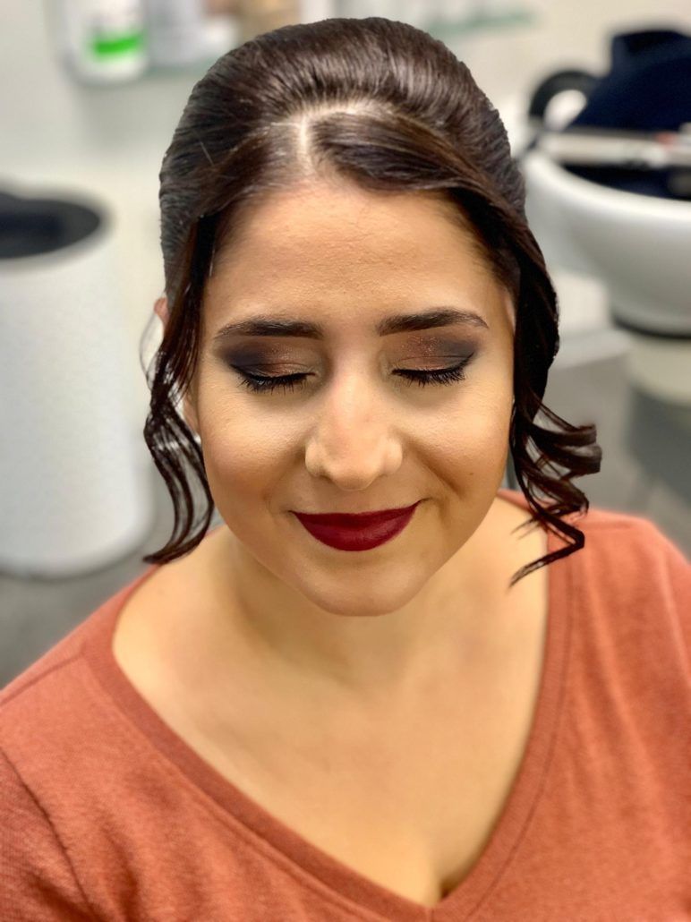 Eine Frau, die ein rotes Hemd und roten Lippenstift trägt, lächelt mit geschlossenen Augen.