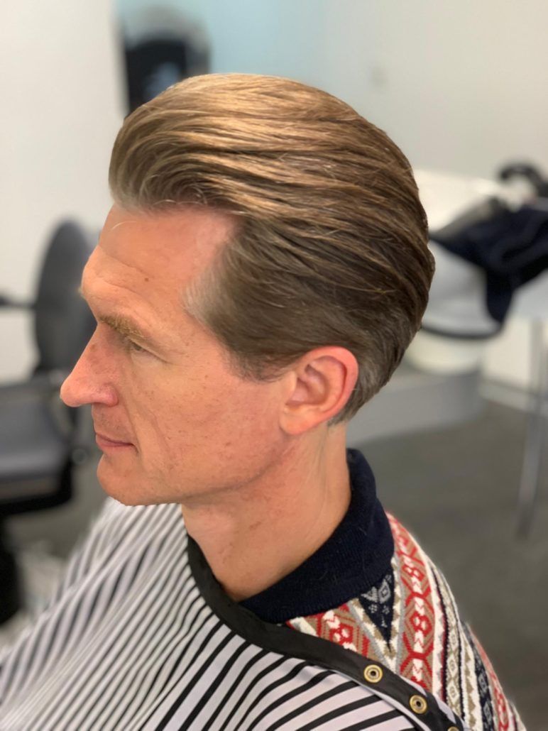 Ein Mann in einem gestreiften Hemd lässt sich die Haare schneiden