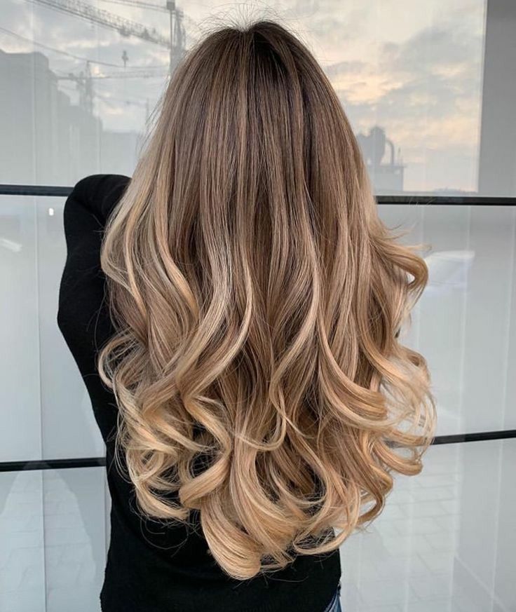 Eine Frau mit langen, welligen blonden Haaren trägt einen schwarzen Pullover.