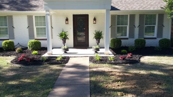 Front entrance of a house with a walkway, porch columns, and potted plants