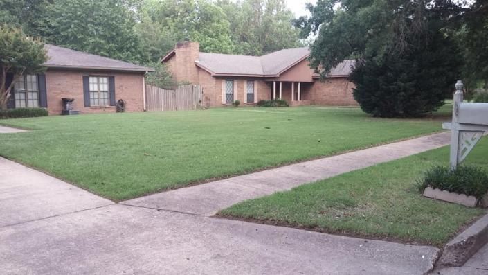 Brick suburban house with a large green lawn and concrete driveway under overcast skies