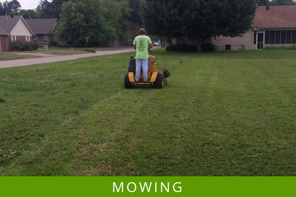 Person mowing a grassy lawn with a riding mower in a suburban yard