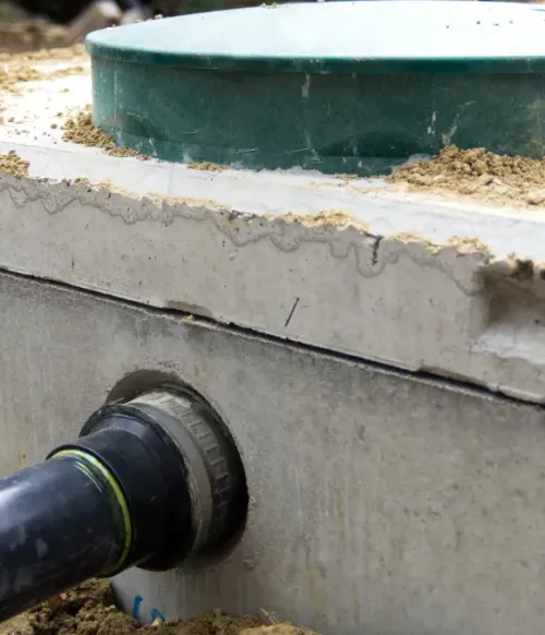 Black pipe entering a concrete tank wall below a green circular opening with debris around the rim