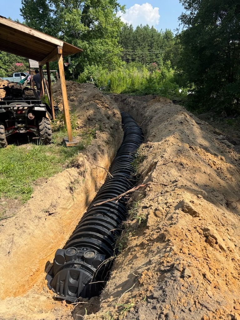 Black corrugated pipe laid in a dirt trench at a construction site beside a wooded hillside