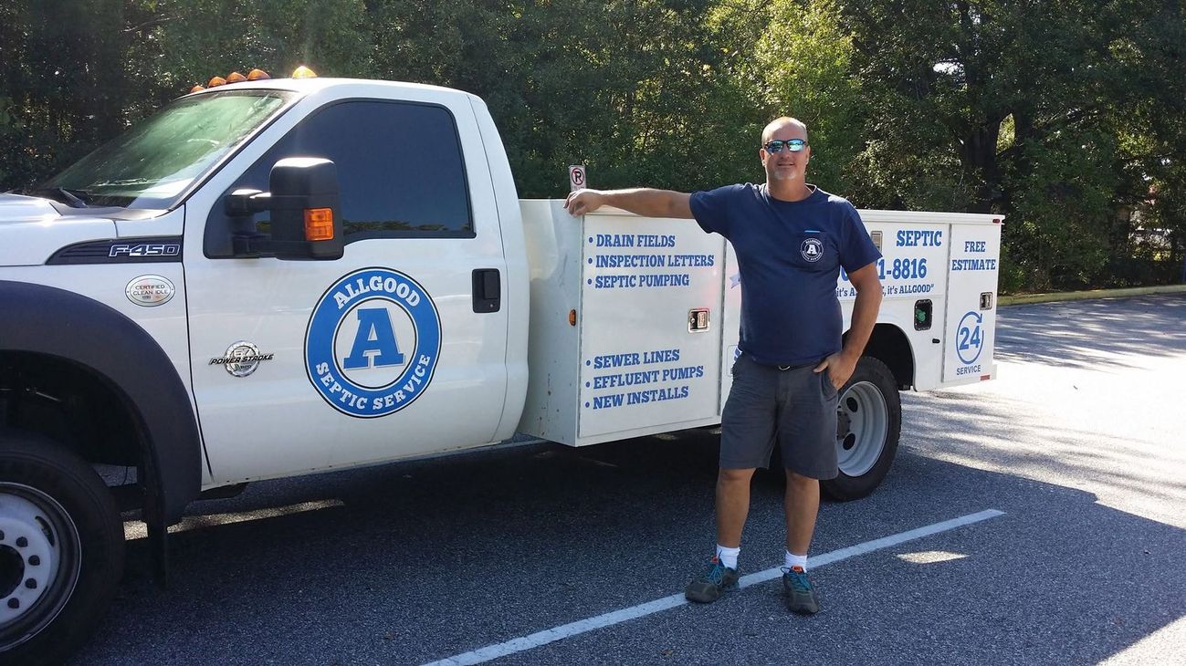 Man standing beside a white utility truck with blue logos and signage on a sunny street.