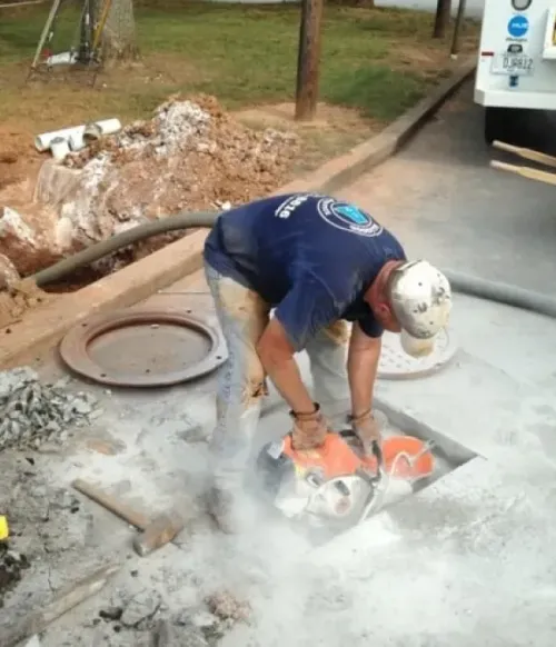 Worker using a power saw to cut pavement on a roadside construction site