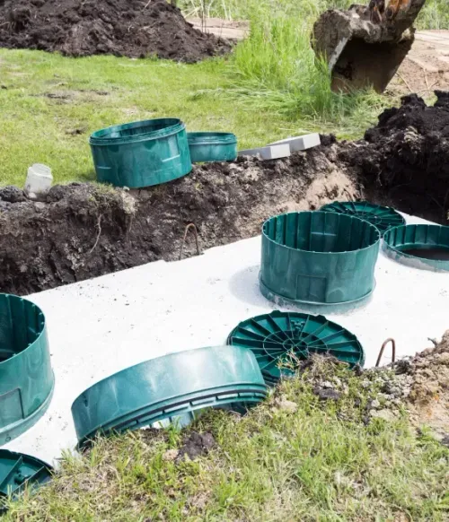 Green utility rings and lids scattered in a muddy trench beside a white slab outdoors