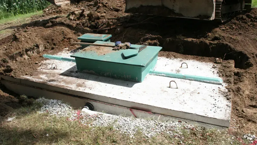 Concrete septic tank cover with green access hatch in a dirt excavation outdoors