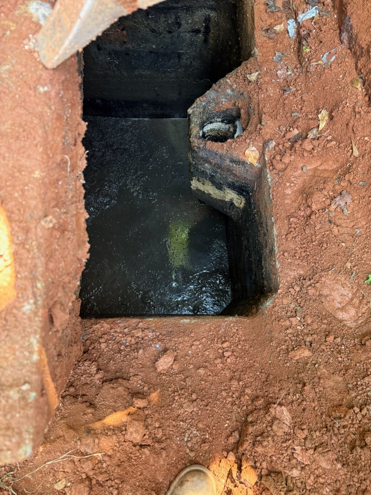 Open muddy pit with dark water and a small pipe embedded in the earthen wall