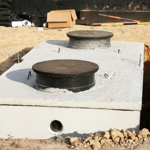 Concrete utility vault with two round black covers in a dirt construction area
