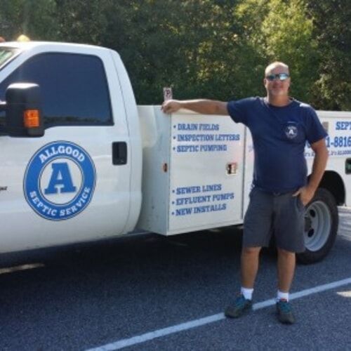 Service truck with Allgood Plumbing logo and a man standing beside it on a roadside.