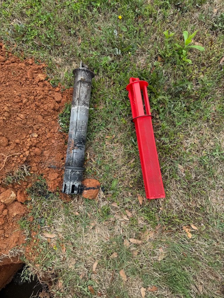 Red and black pipe pieces lying on grass beside a patch of exposed soil.