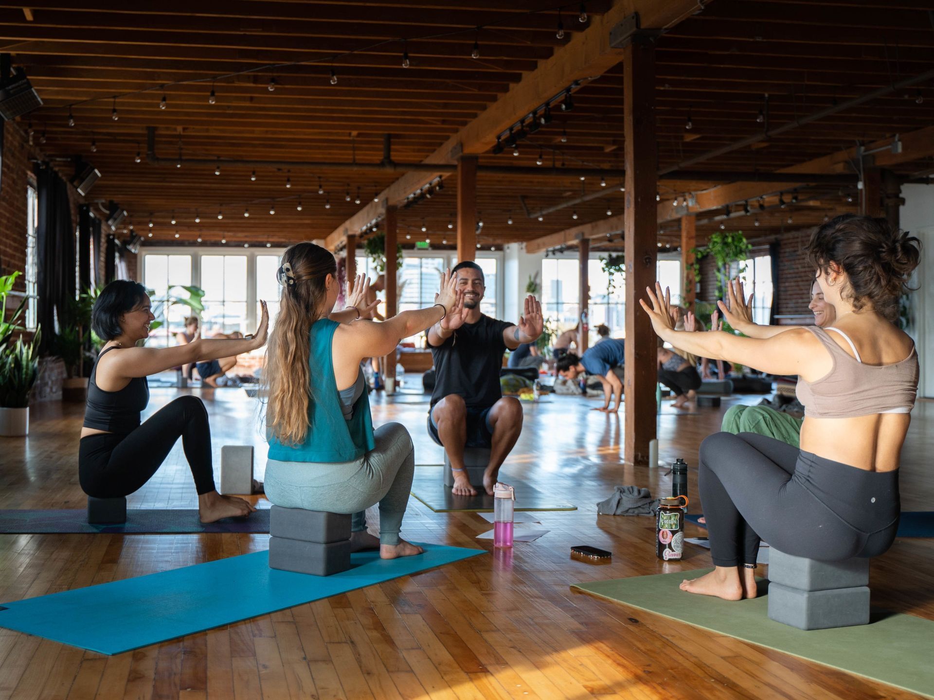People practicing yoga on mats and blocks in a bright studio with wooden beams.
