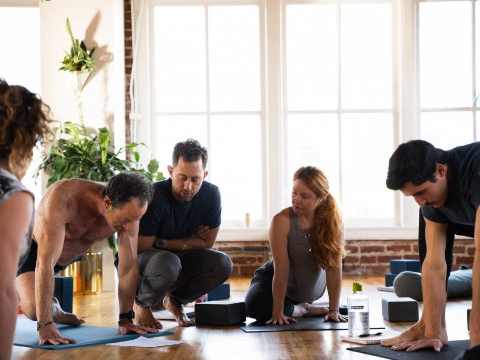 People on yoga mats in a bright studio, gathered around a small black bowl and water bottles.