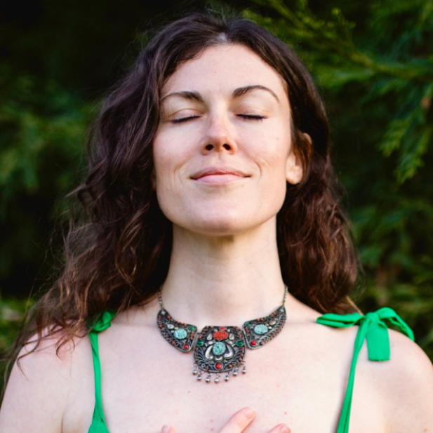 Woman with closed eyes wearing an ornate necklace against a green outdoor background