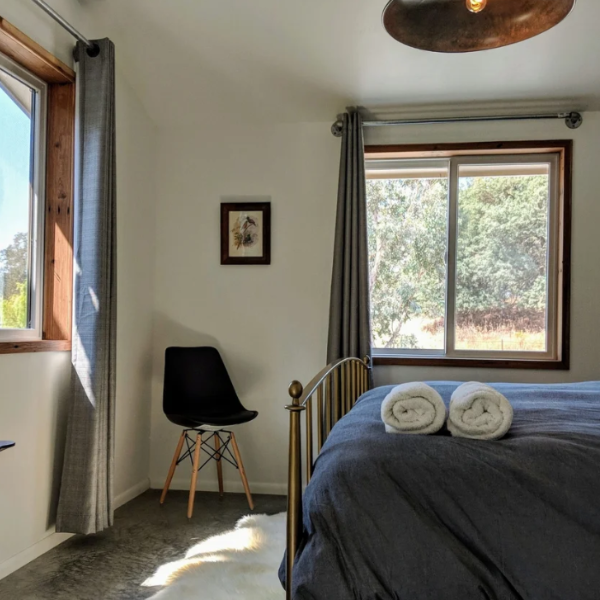 Bright bedroom with bed, rolled towels, black chair, and sunlight through two windows