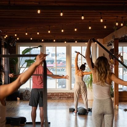 People stretching in a warm-lit yoga studio with large windows and hanging lights