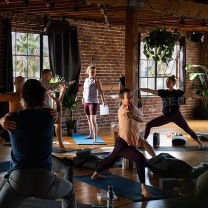 Yoga class practicing poses in a sunlit brick studio with plants and mats