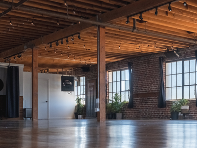 Empty industrial loft with exposed brick, wooden beams, large windows, and polished concrete floor