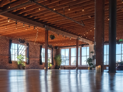 Spacious empty loft with exposed brick, wood ceiling beams, large windows, and polished concrete floor