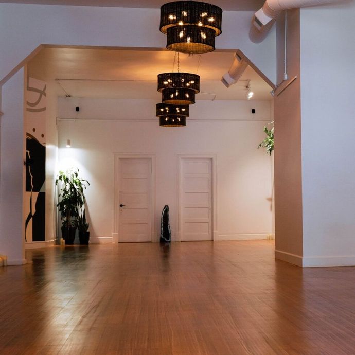Empty modern gallery room with wooden floors, white walls, and hanging chandeliers